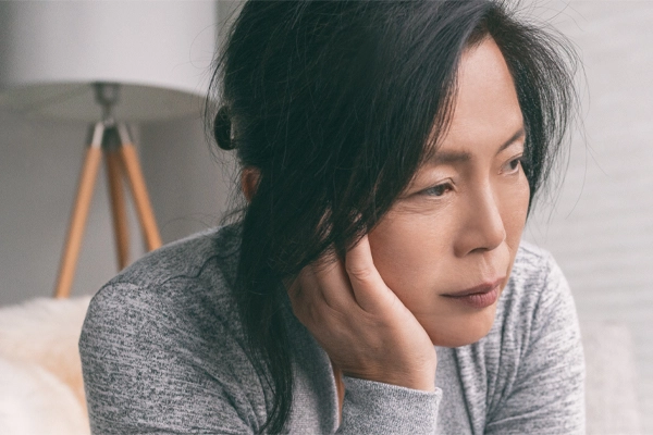 Adrenal-Fatigue-Doctor A middle-aged asian woman sitting on her couch, resting her head on her hand, suffering from adrenal fatigue. Get treatment for adrenal fatigue syndrome from Allen Green, M.D. of Center for Optimum Health in Los Angeles.