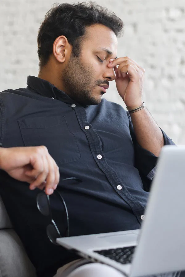Adrenal-Fatigue-Treatment A middle-aged man with a laptop closing his eyes and rubbing his nose. He needs treatment for Adrenal Fatigue Syndrome from Allen Green, M.D. of Center for Optimum Health in Los Angeles.
