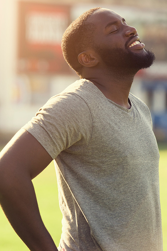 A black man in a t-shirt smiles and raises his face to the sun due to relief from allergies. Get treatment for allergic rhinitis from Allen Green, M.D. of Center for Optimum Health in Los Angeles.