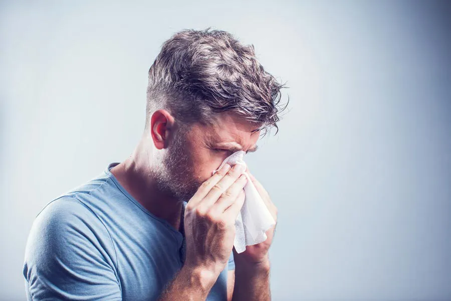 A man in a gray shirt blows his nose. Get help for allergies from Allen Green, M.D. of Center for Optimum Health in Los Angeles.