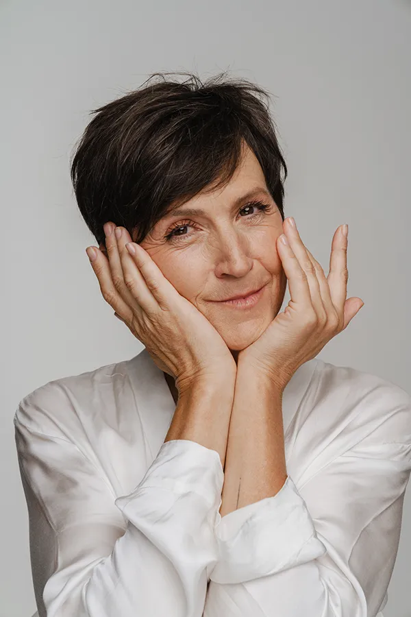 A middle-aged woman with short brown hair touches her face after successful angioedema treatment from Allen Green, M.D. of Center for Optimum Health in Los Angeles.