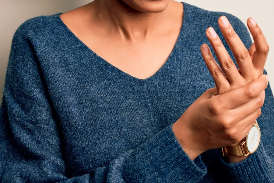Close up of a woman in a blue sweater massaging one aching hand with the other. Get help for arthritis from Allen Green, M.D. of Center for Optimum Health in Los Angeles.
