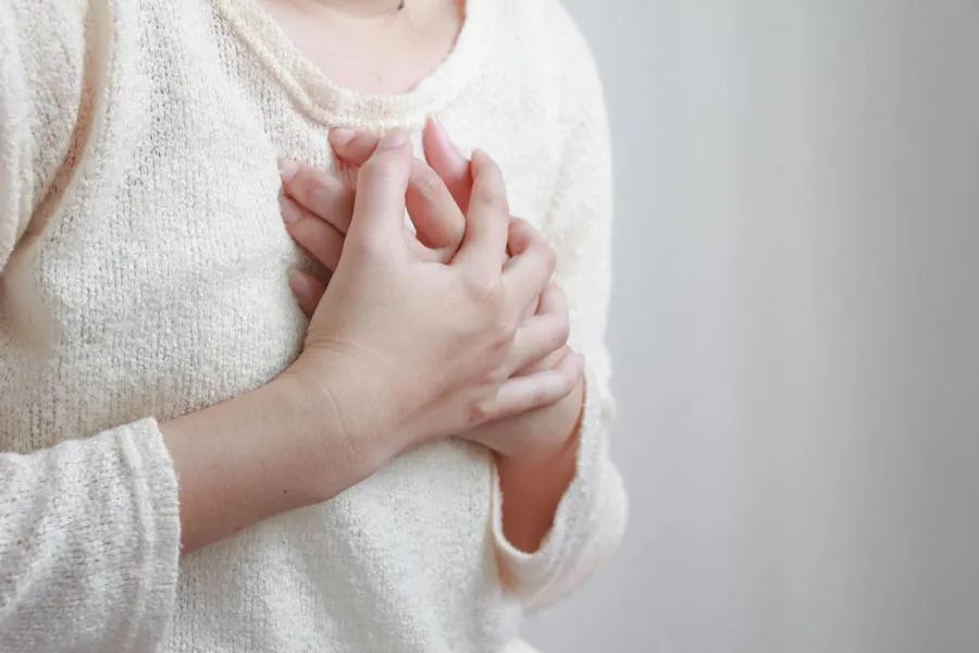Close-up of a woman in a white sweater clutching her chest in respiratory distress. Get treatment with asthma from Allen Green, M.D. of Center for Optimum Health in Los Angeles.