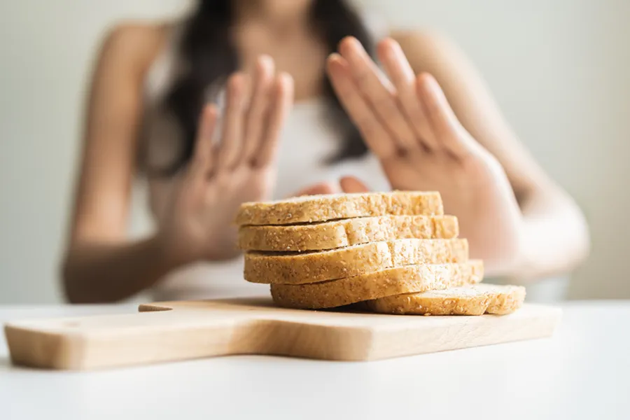 Close up of a stack of bread slices on a cutting board with a woman's hands behind them, refusing to eat. Get treatment for Celiac Disease from Allen Green, M.D. of Center for Optimum Health in Los Angeles.