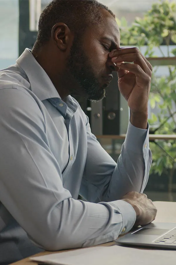Chronic-Fatigue-Treatment A black man rubbing the top of his nose at his desk, in need of chronic fatigue treatment from Allen Green, M.D. of Center for Optimum Health in Los Angeles.