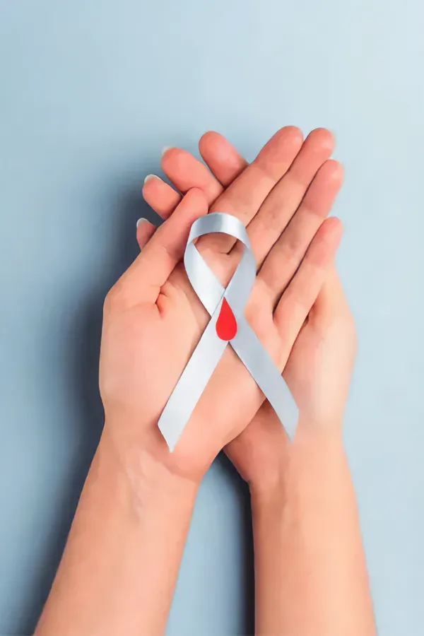 A woman's hands holding a white ribbon with a red drop symbol on it, symbolizing diabetes treatment from Allen Green, M.D. of Center for Optimum Health in Los Angeles.