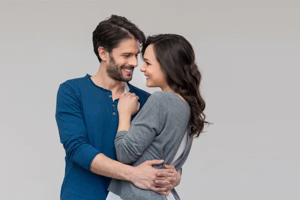 A man in a blue shirt embracing a woman in a gray shirt smiles due to his successful erectile dysfunction care from Allen Green, M.D. of Center for Optimum Health in Los Angeles.