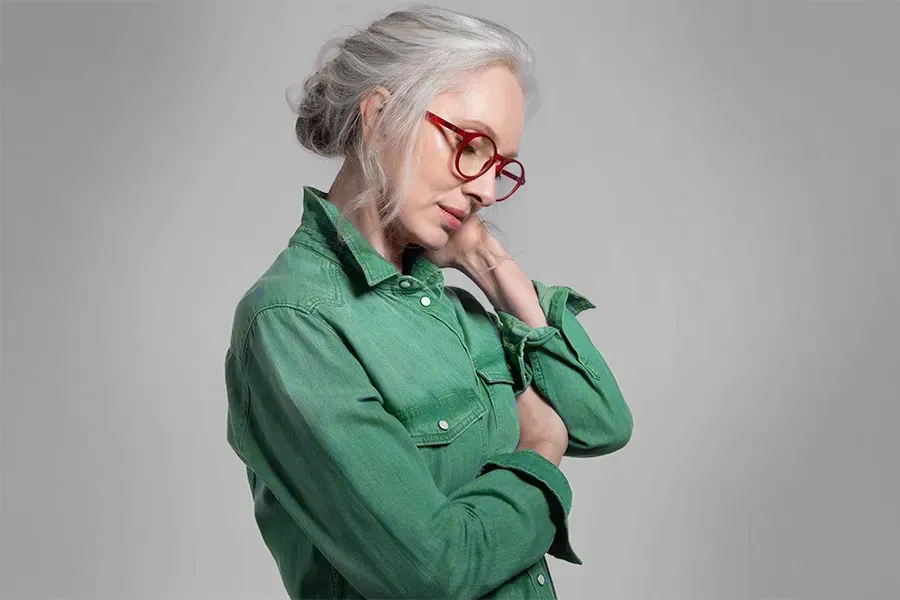 An older woman with glasses wearing a green shirt holds her forehead, experiencing pain. Schedule Low Dose Naltrexone treatment from Allen Green, M.D. of Center for Optimum Health in Los Angeles.