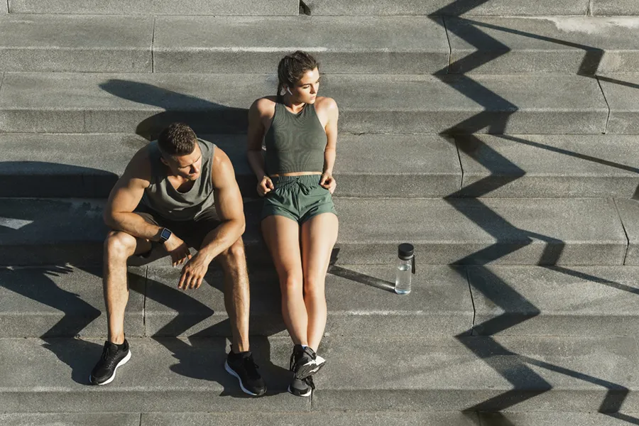 A couple in gray and green track clothes resting after a workout on stone steps, happy with their weight loss plans from Allen Green, M.D. of Center for Optimum Health in Los Angeles.