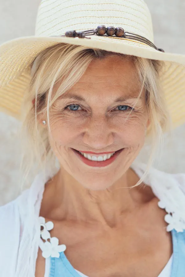A beautiful, smiling older woman with blonde hair and a sunhat, happy with menopause treatment from Allen Green, M.D. of Center for Optimum Health in Los Angeles.