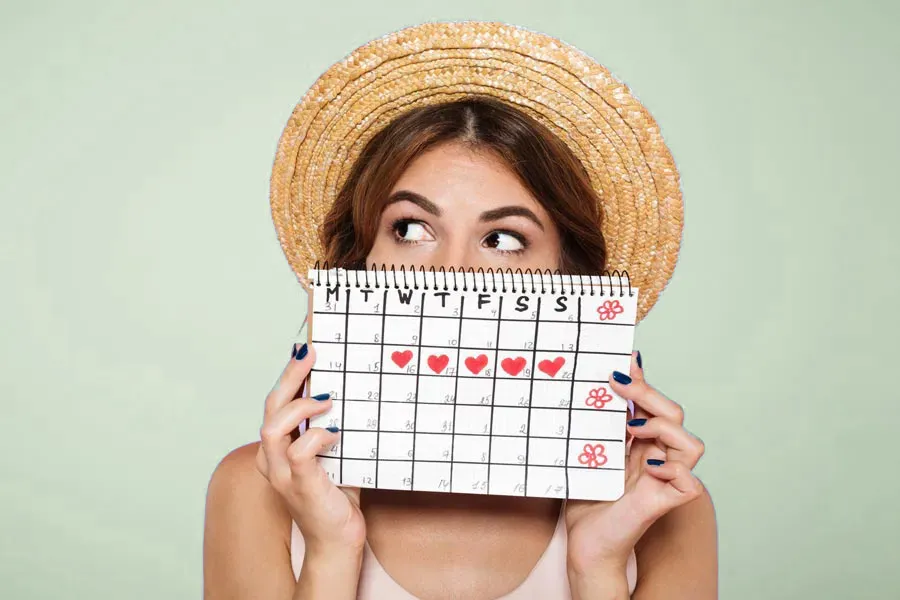 A woman in a straw hat holds a calendar with several days marked off in front of her nose and mouth. Get treatment for menstrual dysfunction from Allen Green, M.D. of Center for Optimum Health in Los Angeles.