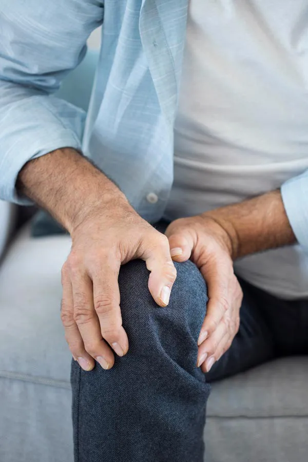 A close-up of a man holding his knee while experiencing pain from osteoporosis. Get osteoporosis treatment from Allen Green, M.D. of Center for Optimum Health in Los Angeles.