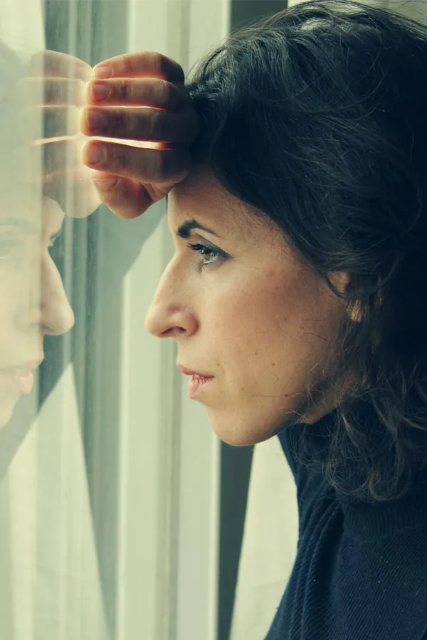 A brunette woman in a thin dark turtleneck looks out the window with a serious expression, suffering from PCOS. Get treatment for Polycistic Ovarian Syndrome/PCOS from Allen Green, M.D. of Center for Optimum Health in Los Angeles.