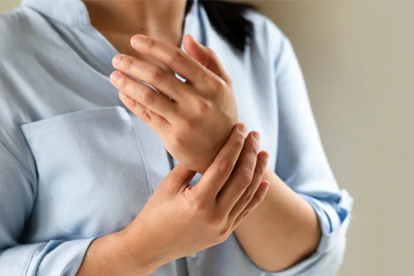 Close up of a woman in a blue blouse rubbing her wrist. Get rheumatoid arthritis treatment from Allen Green, M.D. of Center for Optimum Health in Los Angeles.