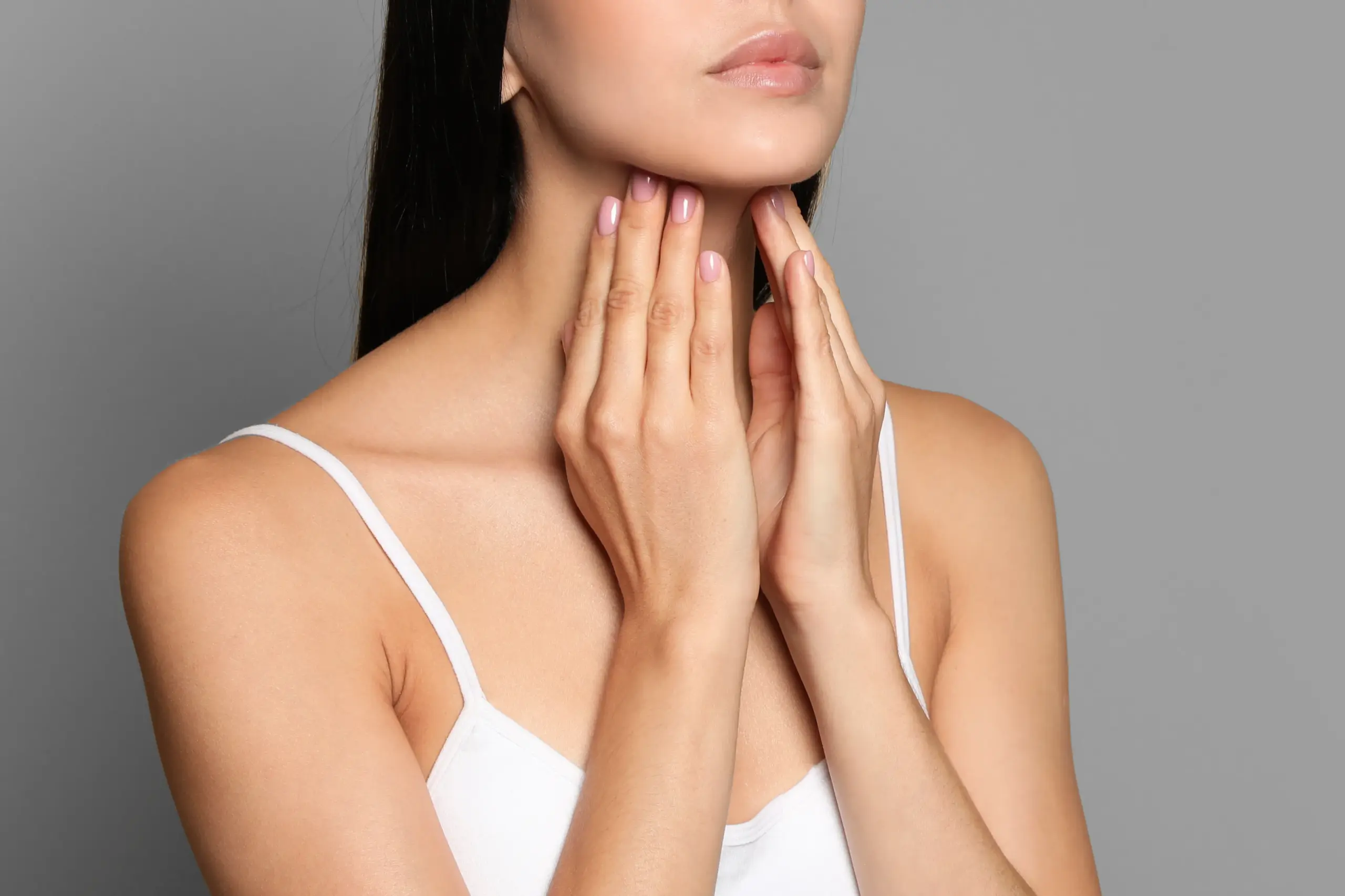 A woman in a white tank top touches her neck looking for signs of thyroid disorder. Get help for thyroid disorders from Allen Green, M.D. of Center for Optimum Health in Los Angeles.