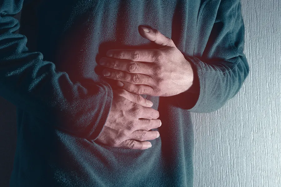 Close-up of the midsection of a man in a green sweater clutching his gut in pain. Get treatment for Ulcerative Colitis from Allen Green, M.D. of Center for Optimum Health in Los Angeles.